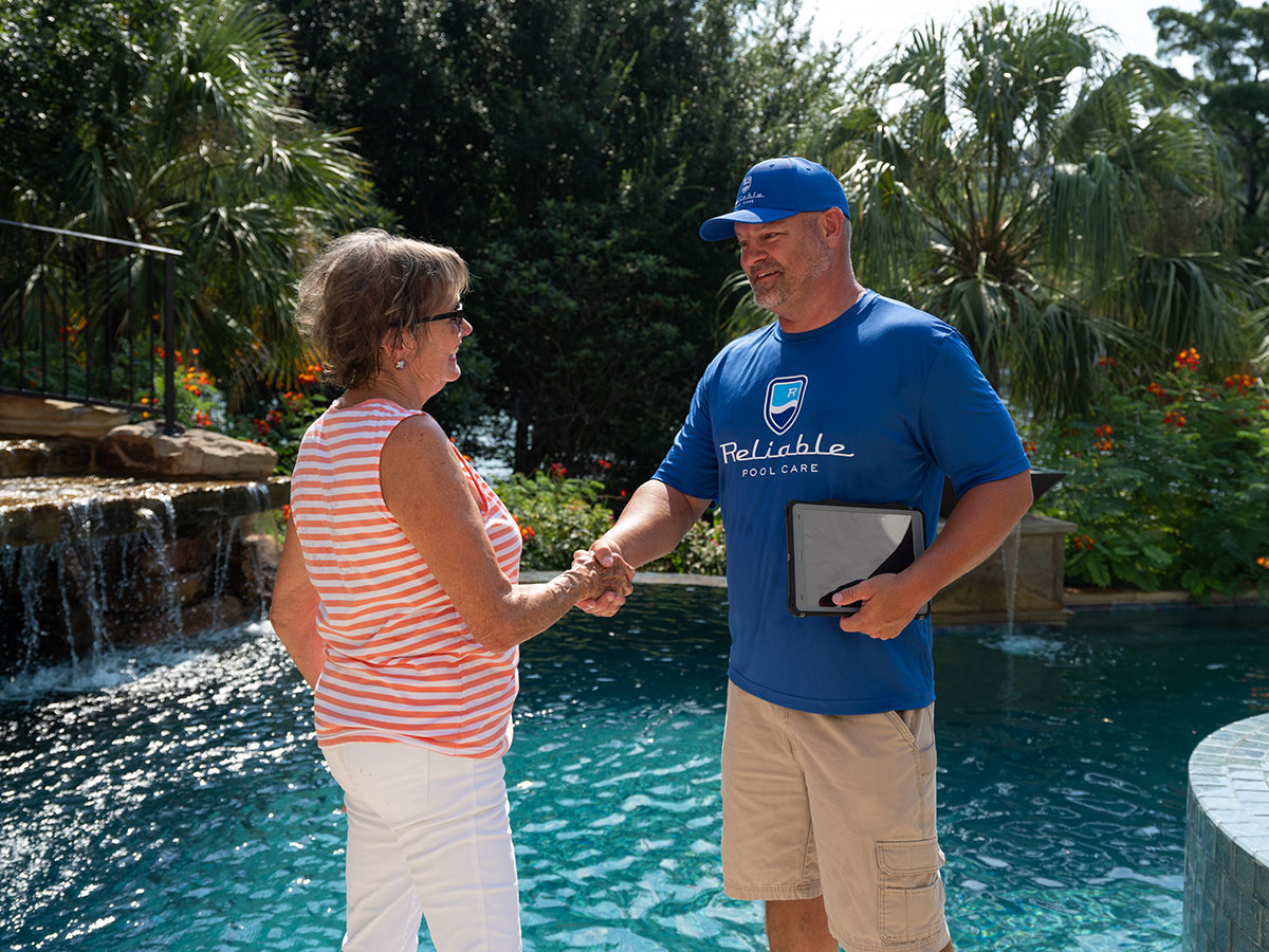 a Reliable pool care technician meeting with a customer shaking hands holding a tablet device in front of a pool